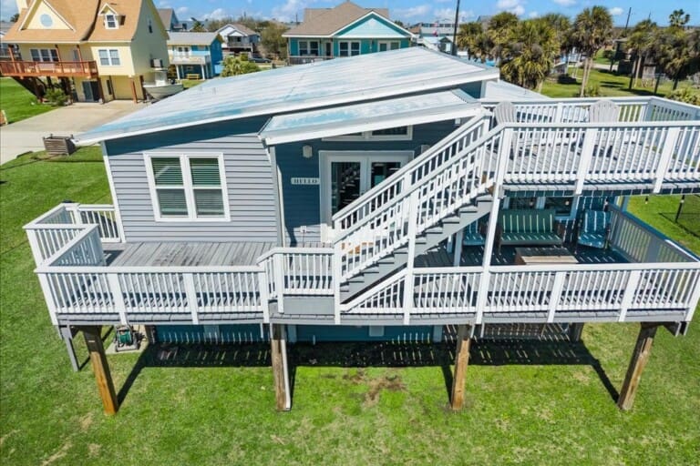 Elevated vacation rental home on stilts with large wraparound deck and white railings, Jamaica Beach Texas