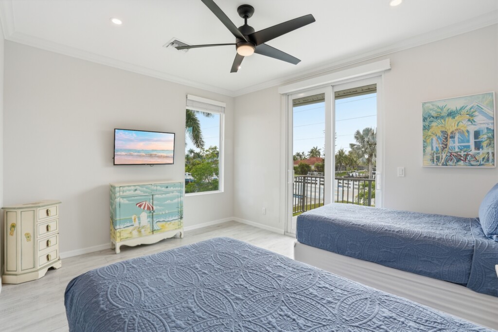 Bright coastal twin bedroom with balcony access and palm-view natural light at Tigertail Beach Villa, Marco Island FL